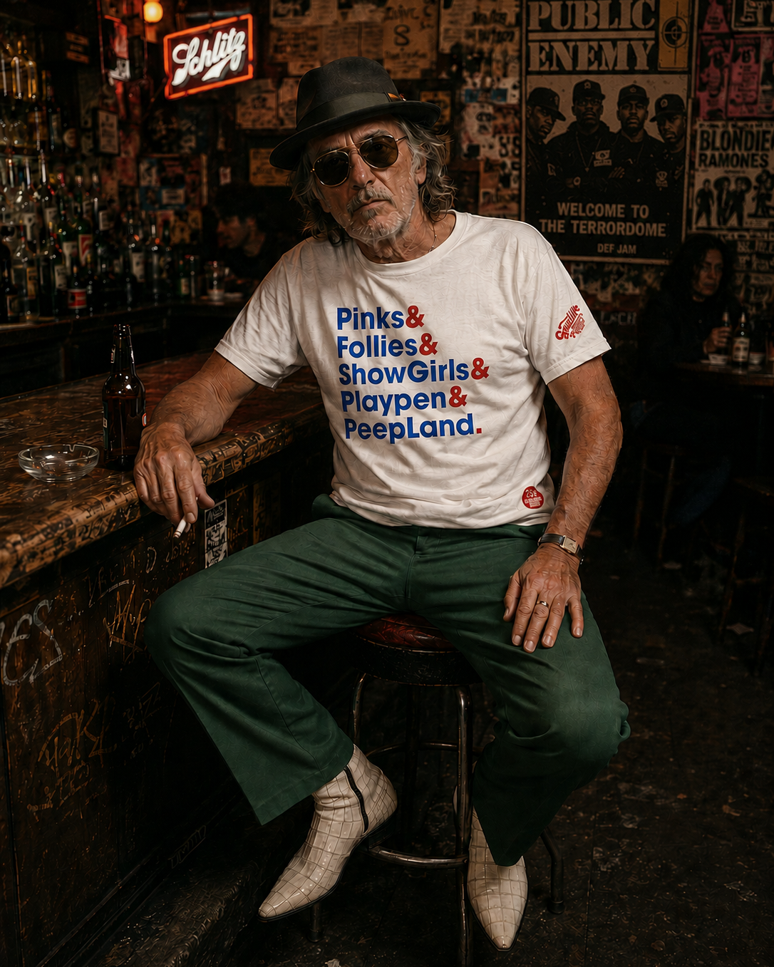 Man in a white Smutlife Tourist Destination T-shirt with red and blue text, green pants, and white boots, sitting at a bar.