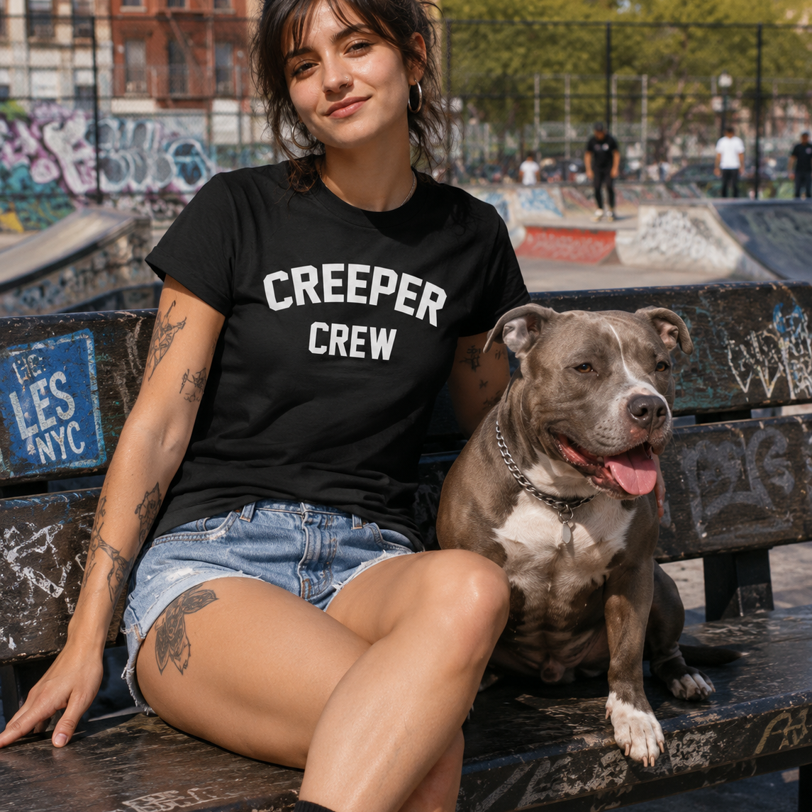 Woman in black "CREEPER CREW" tee, denim shorts, and a gray pit bull on a park bench.
