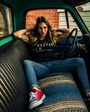 Woman in black SMUTLIFE "CREEPER CREW" cotton tee and blue jeans, sitting in a vintage teal truck.