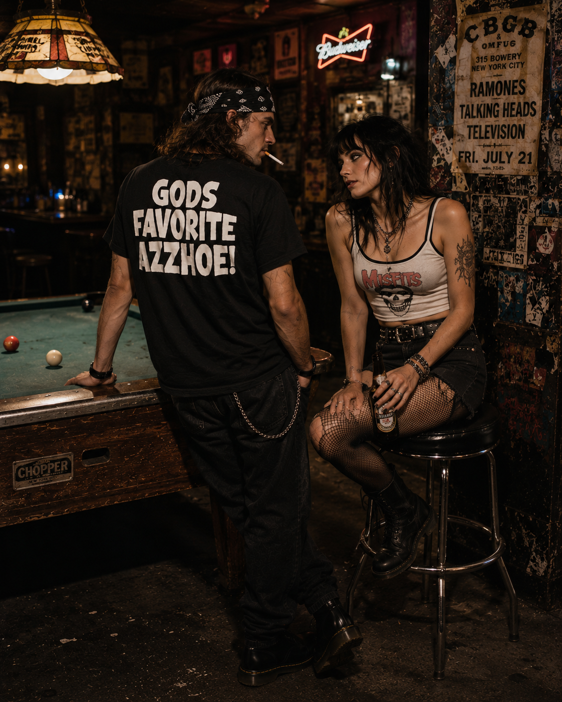 Man in black "GODS FAVORITE AZZHOE" t-shirt leans on a pool table, looking at a woman in a white Misfits crop top.