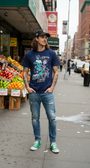 Man in navy "Livin' La SMUTLIFE Loca" alien fiend graphic tee, distressed jeans, and green sneakers.