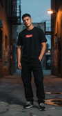 Man wearing a black SMUTLIFE NYC script felt unisex t-shirt with a red box logo, black cargo pants, and sneakers.