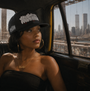 Woman in a black SMUTLIFE THROWIE 6-panel snapback hat, looking out a taxi window at the NYC skyline.