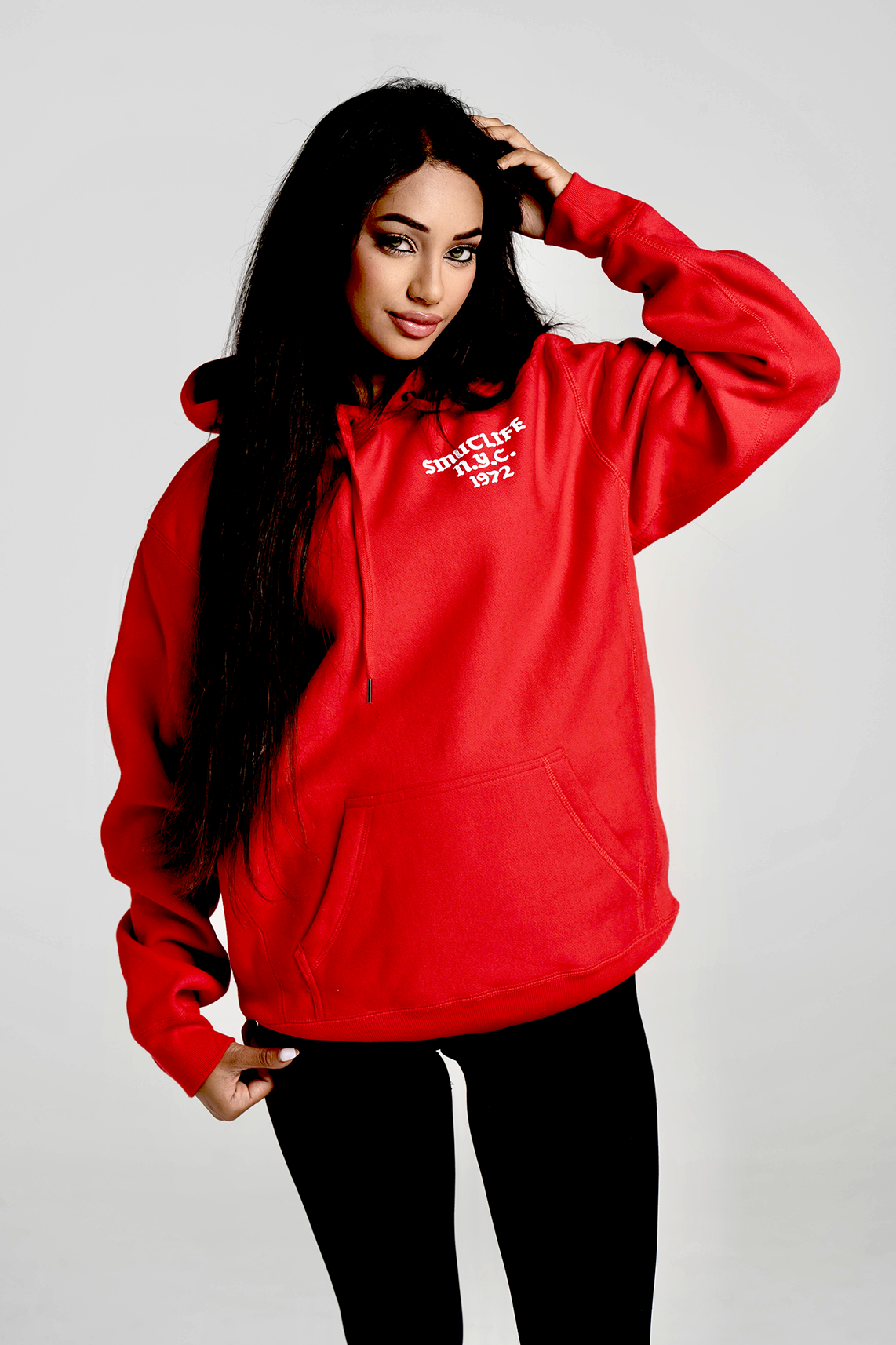 Woman wearing a red SMUTLIFE 1972 N.Y.C. unisex hoodie with a front pouch pocket.