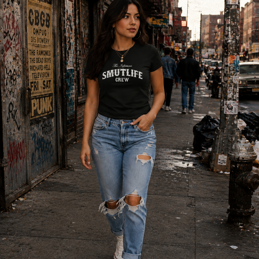 Woman in black "SMUTLIFE CREW" tee, ripped jeans, and white sneakers walking on a city street.