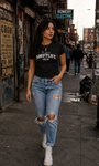 Woman in black "SMUTLIFE CREW" tee, ripped jeans, and white sneakers walking on a city street.
