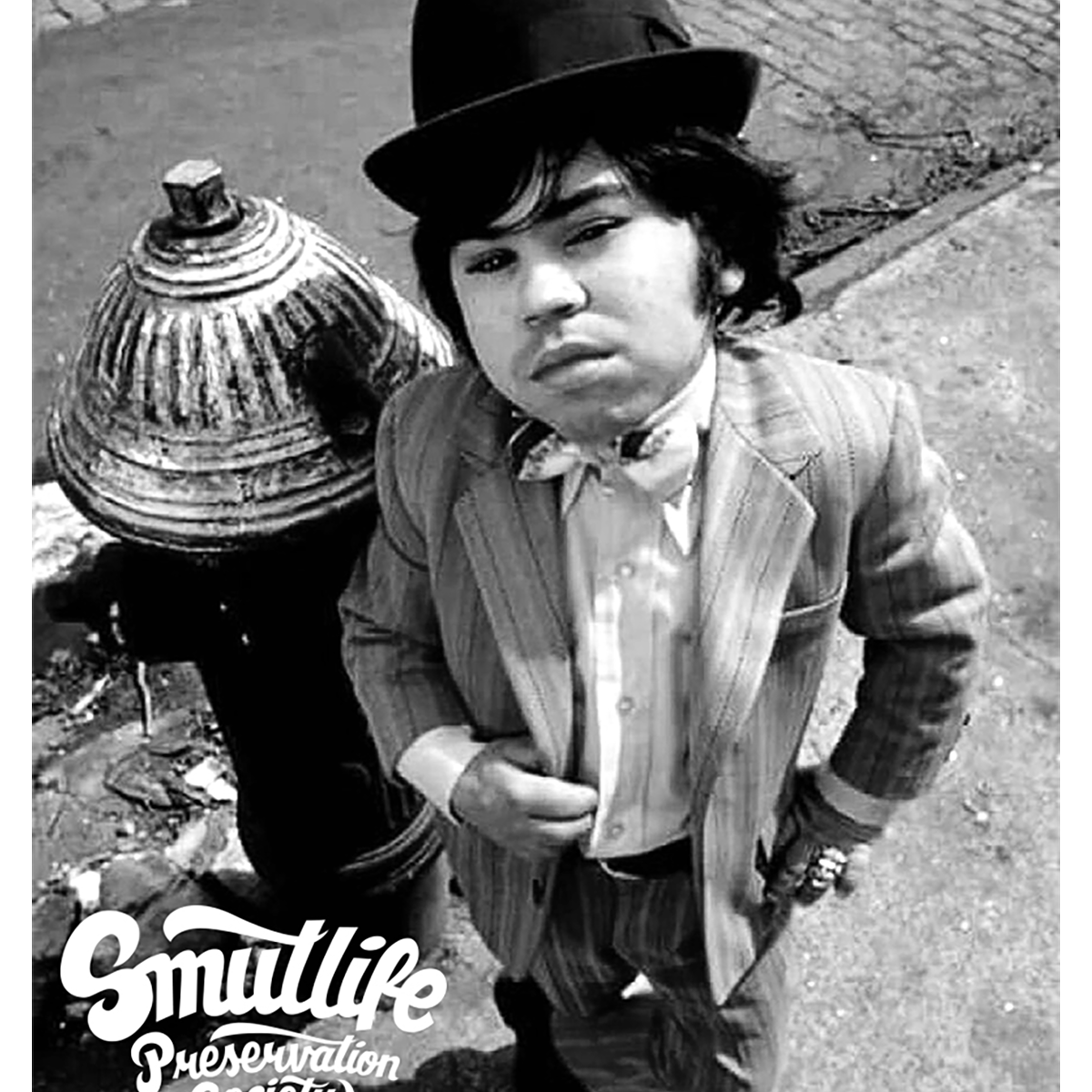 Black and white image of Hervé Villechaize (Tattoo) in a pinstripe suit and bowler hat, standing by a hydrant.