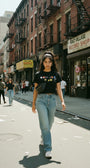 Woman in black SMUTLIFE NYC Subway Crop Top, light wash jeans, and fanny pack walking on a city street.