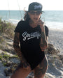 Woman on beach wearing black Smutlife CaliG script t-shirt and matching baseball cap.