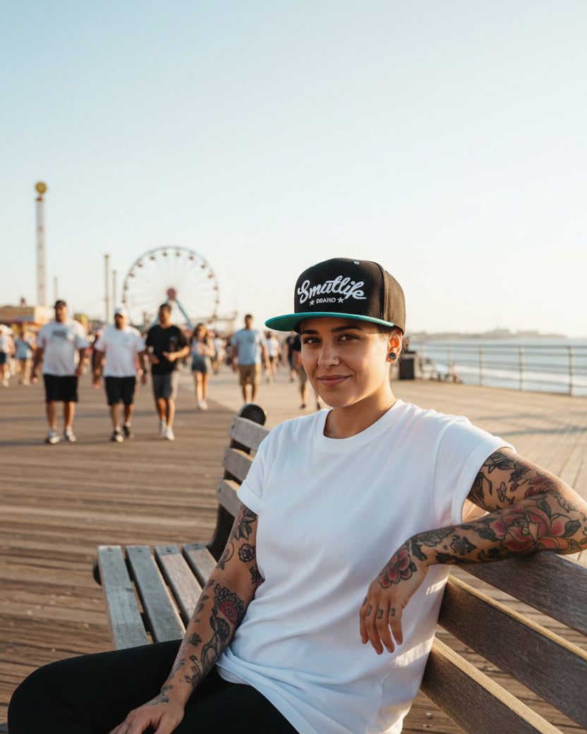 Woman wearing a black and teale Smutlife Tri-Star snapback hat on a boardwalk.