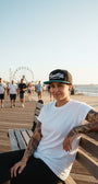 Woman wearing a black and teale Smutlife Tri-Star snapback hat on a boardwalk.