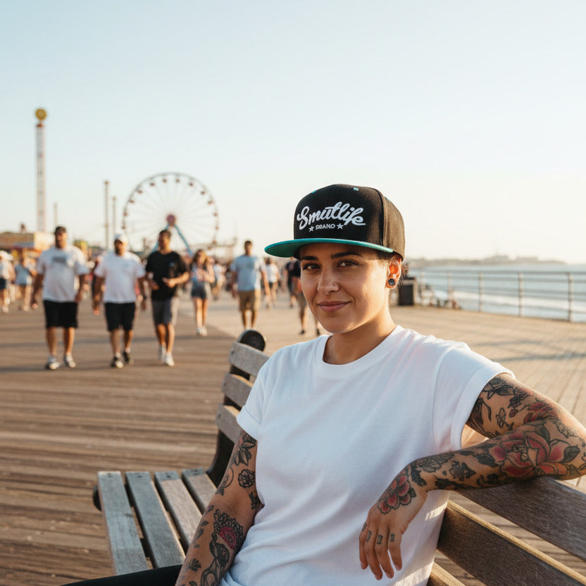 Woman wearing a black and teale Smutlife Tri-Star snapback hat on a boardwalk.