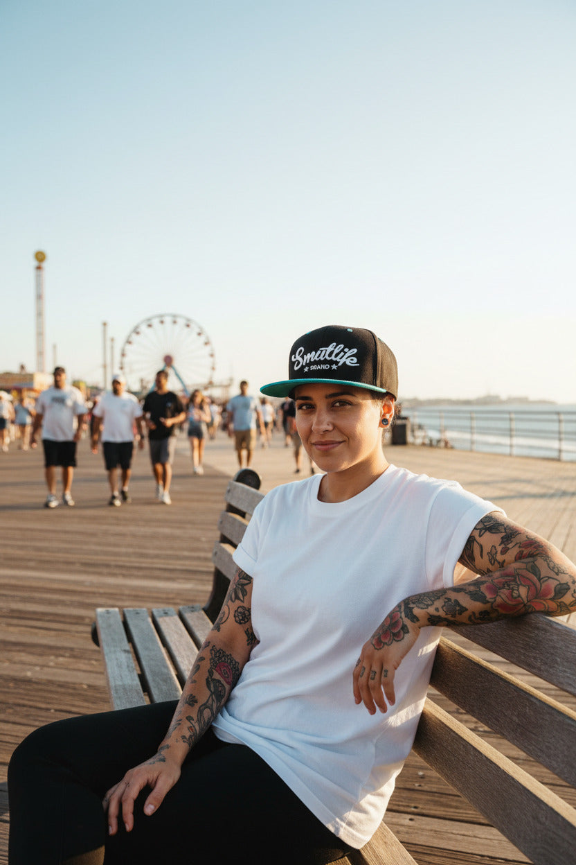 Woman wearing a black and teale Smutlife Tri-Star snapback hat on a boardwalk.